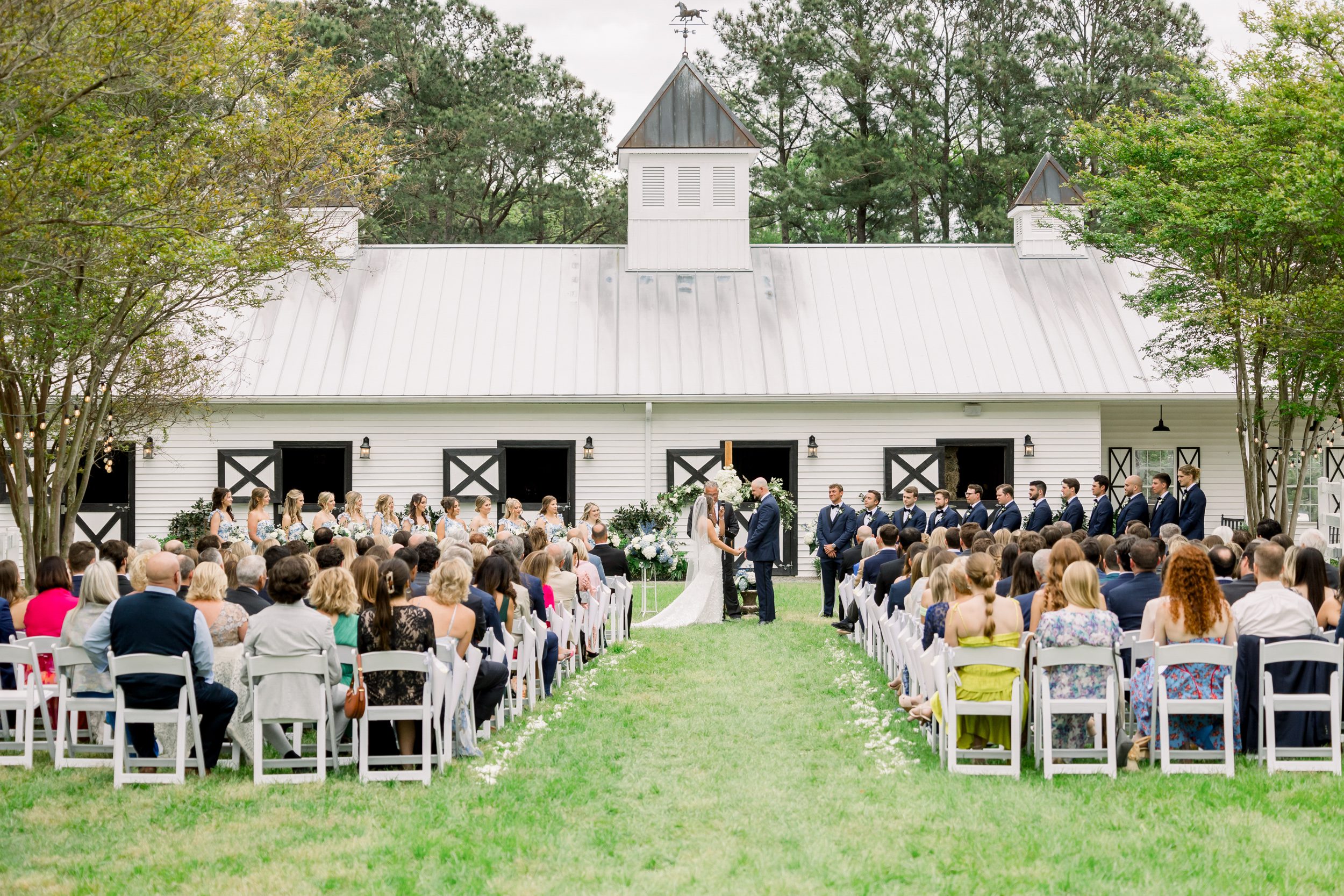 Outdoor wedding ceremony at Sycamore Bend Estate in Wilmington NC surrounded by trees and the backdrop of the barn