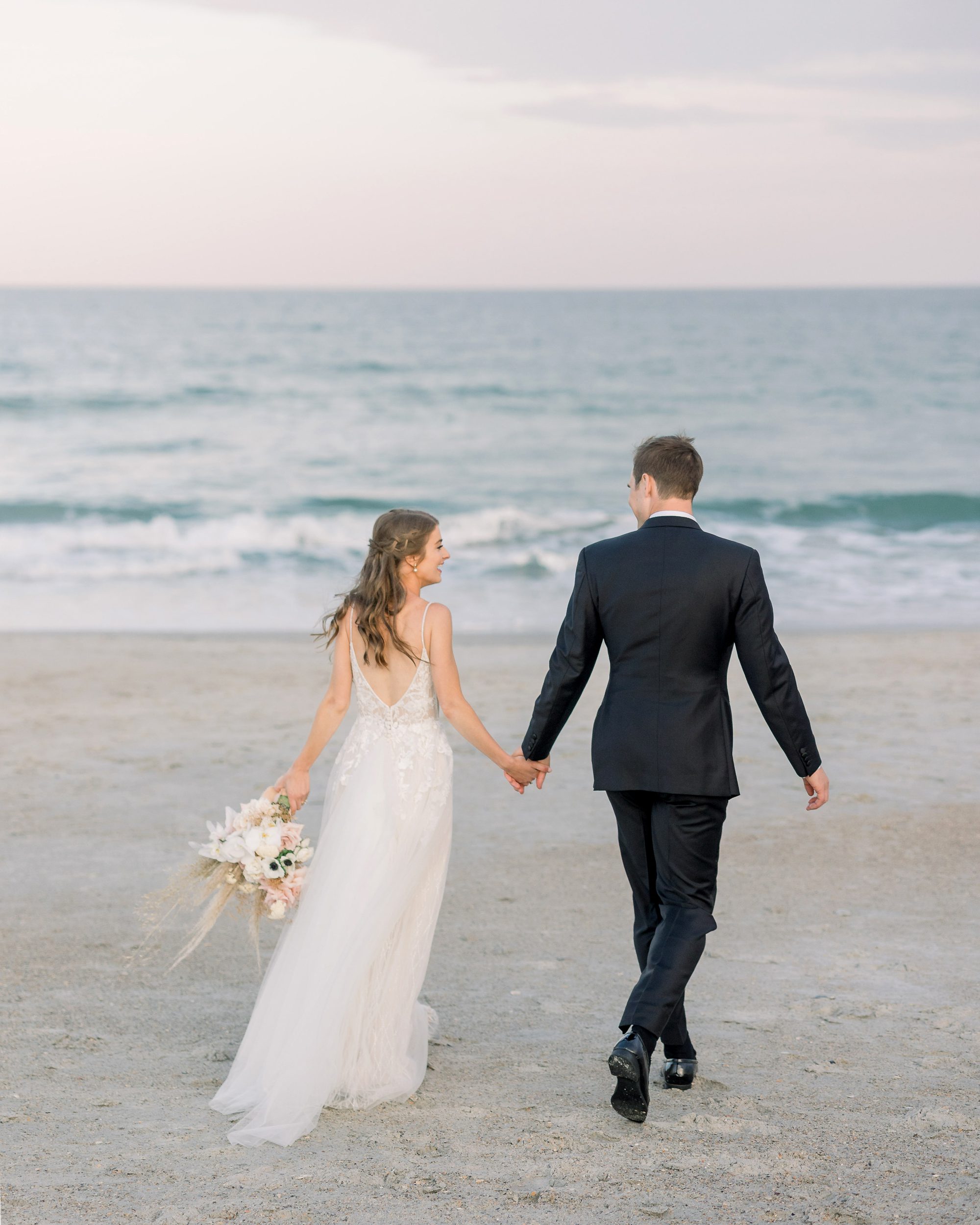 Bride and groom walking together at golden hour on Wrightsville Beach in Wilmington, North Carolina, captured by a Wilmington NC wedding photographer.
