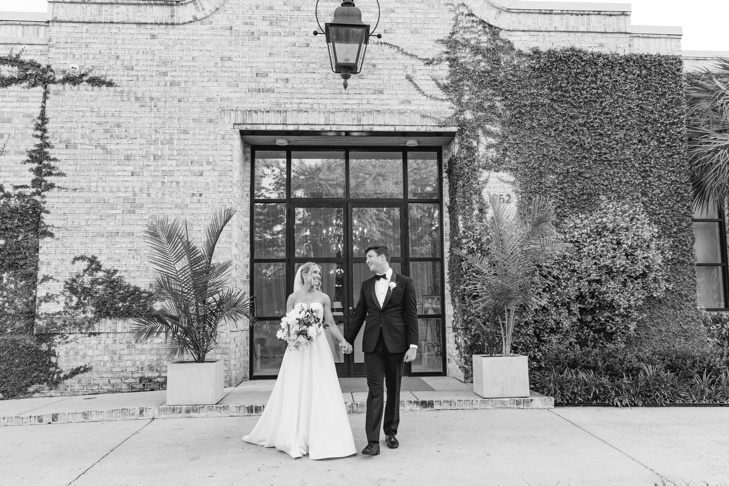 Bride and groom walking hand in hand with the Wilmington, NC wedding venue at Wrightsville Manor in the background