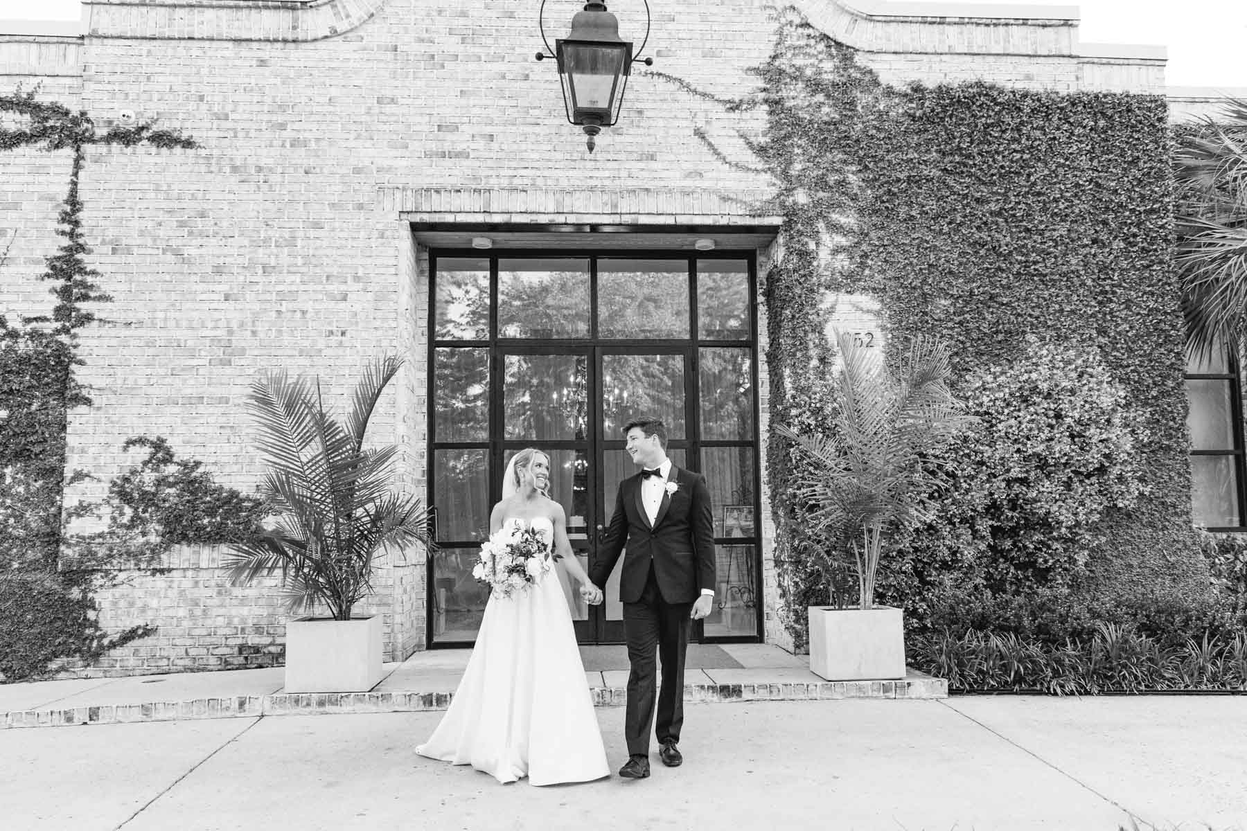 bride and groom walking hand in hand in front of Wrightsville Manor with the venue as the backdrop