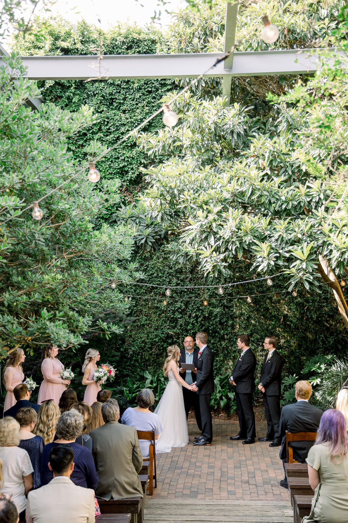 Atrium wedding ceremony under string lights with lush greenery and intimate garden atmosphere
