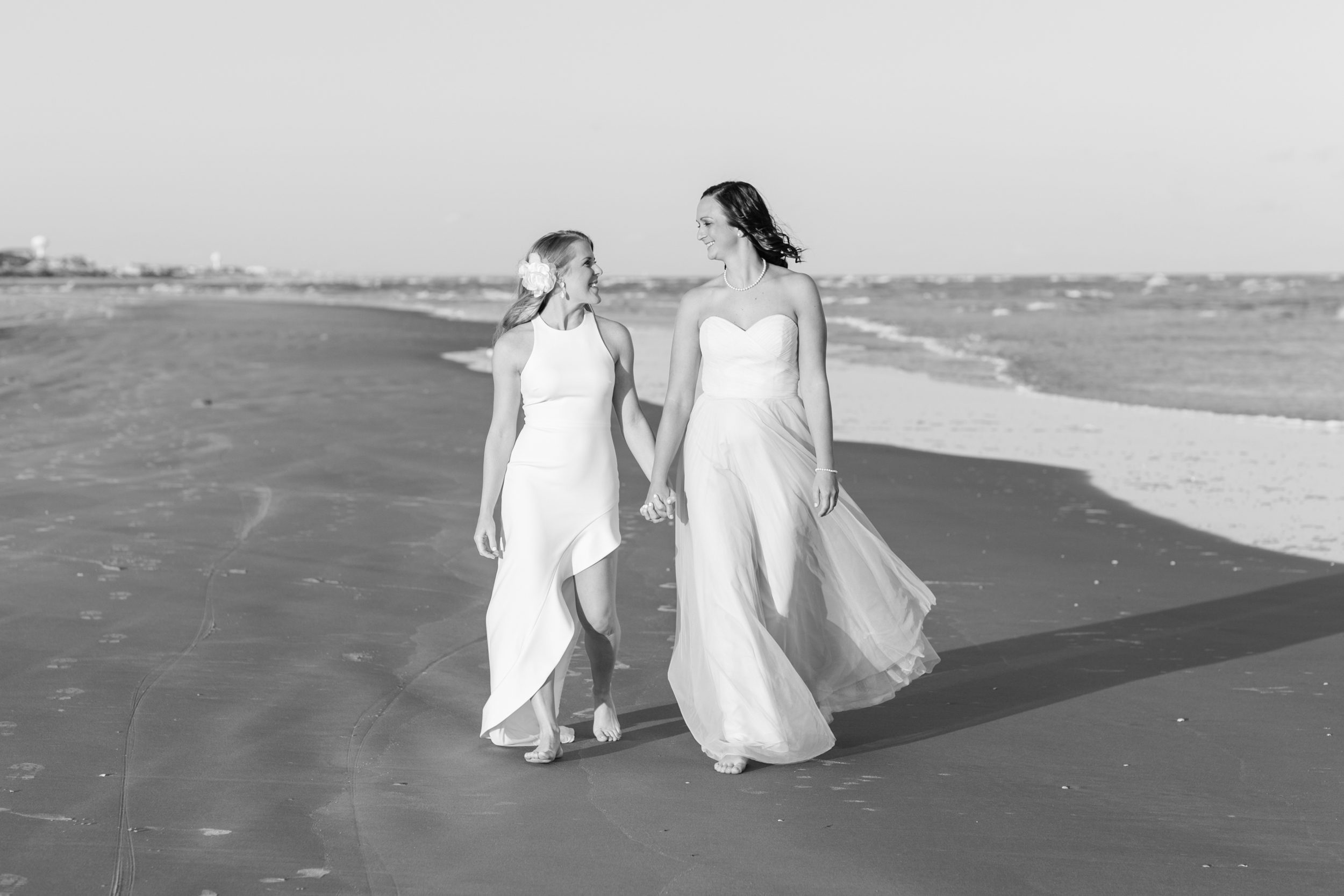 Two brides strolling together on Wrightsville Beach at sunset