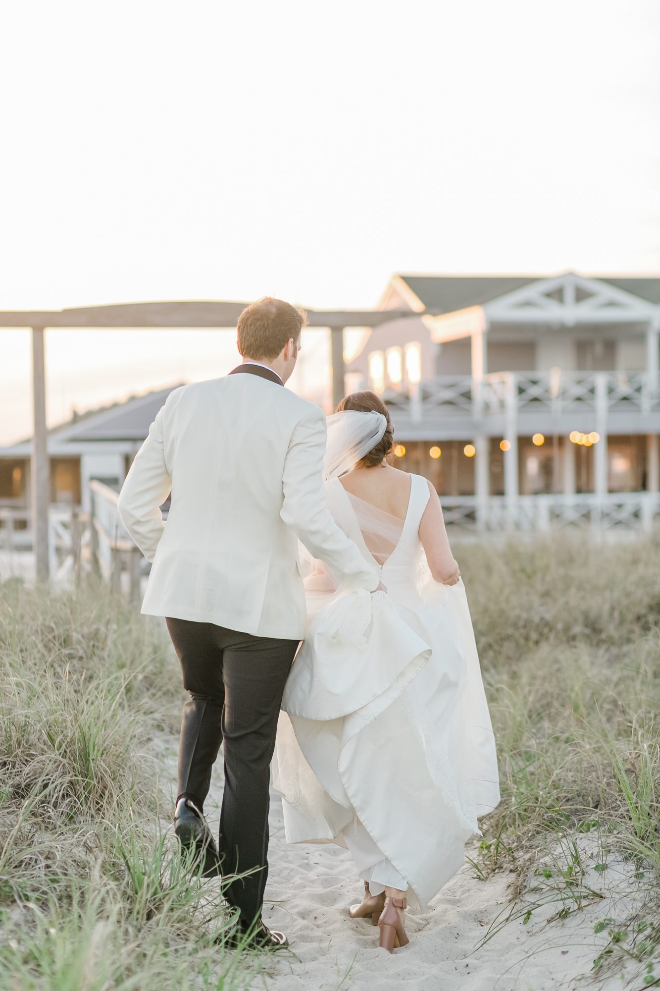 Soft golden hour light as a couple walks along the beach with Carolina Yacht Club behind them